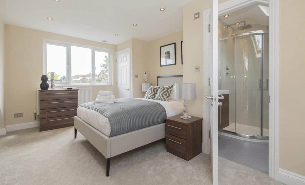 Acton Stylish bedroom featuring a cozy bed with gray accents, bedside tables, neutral walls, and en-suite bathroom access