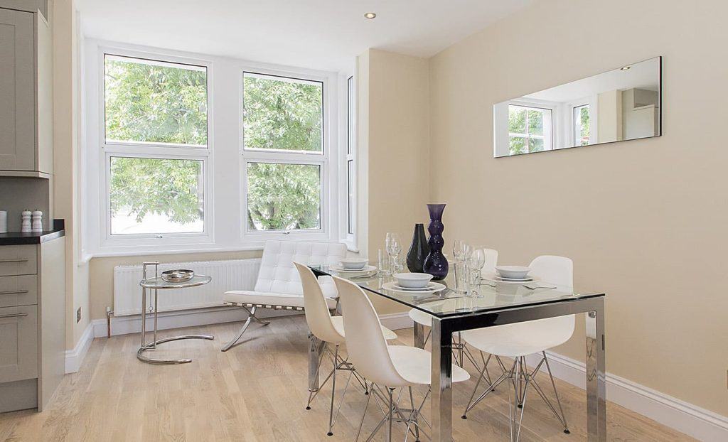 Acton Contemporary dining area with a glass table, white chairs, minimalist decor, and large windows bringing in natural light