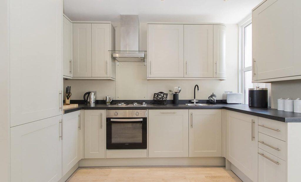 Acton Bright and modern kitchen featuring cream cabinets, a built-in oven, sleek countertops, and a minimalist design