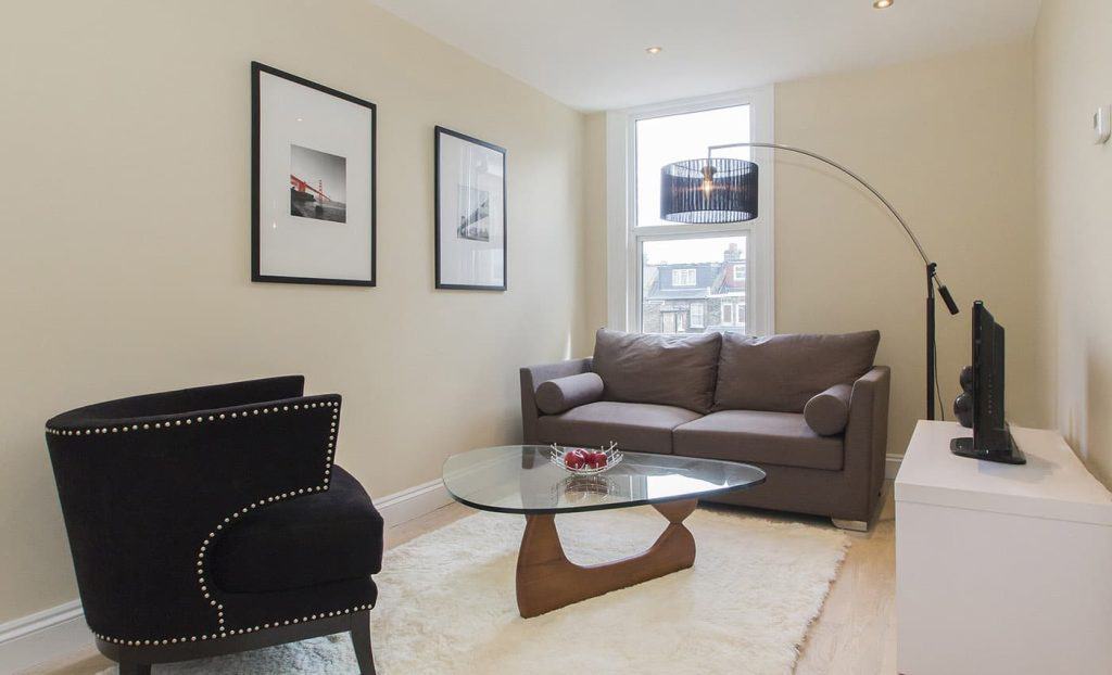 Acton Town House Contemporary living room featuring a gray sofa, glass coffee table, framed wall art, and a cozy rug