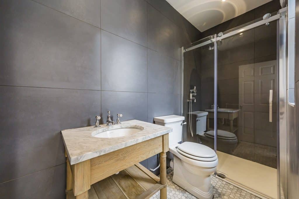 Modern bathroom with glass shower, dark tiled walls, and a wooden vanity unit
