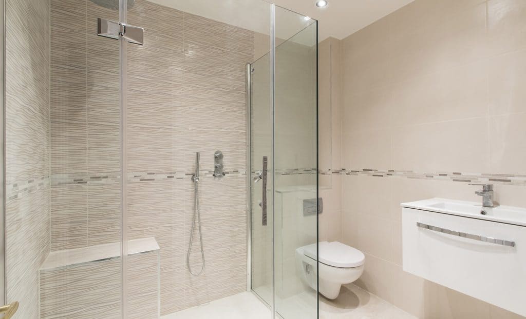 Modern bathroom with glass shower enclosure, beige tiles, and minimalist fixtures